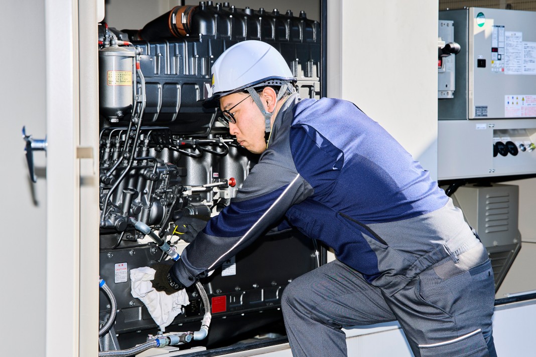 ヘルメットを着用した作業員が、発電機の内部を入念に点検・清掃している様子。